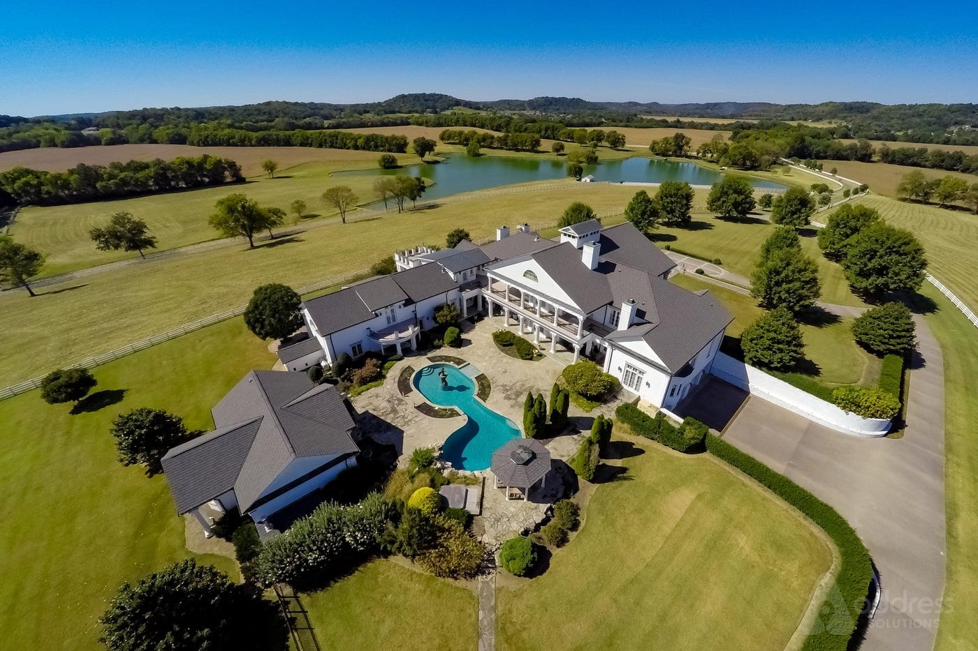 Luxury white farmhouse mansion with lake and green fields